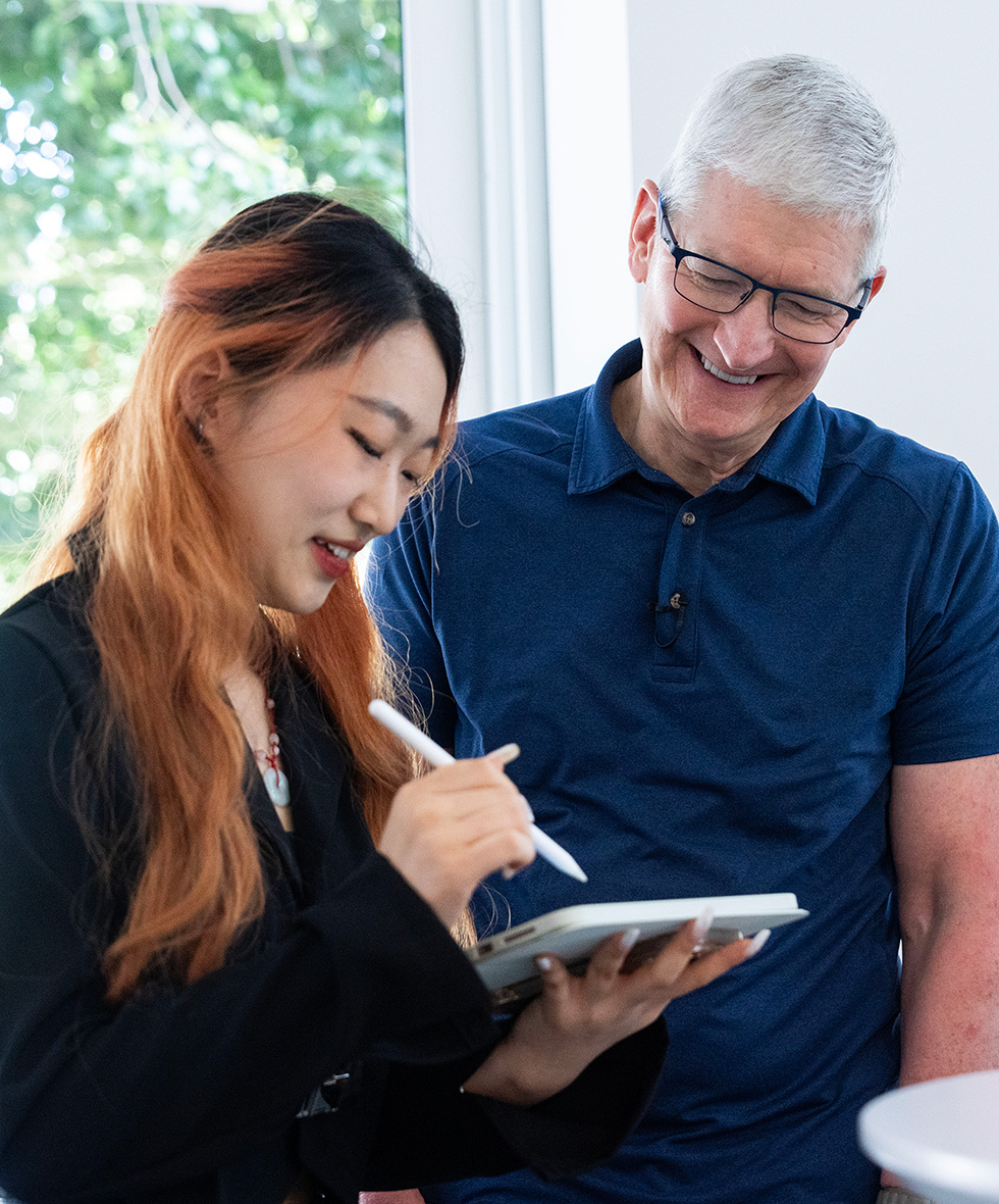 Tim Cook smiles while a Swift Student Challenge winner uses an iPad at WWDC.